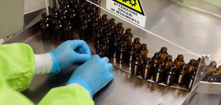 Operatrice CEGS con guanti sistema flaconi in vetro ambrato sul nastro